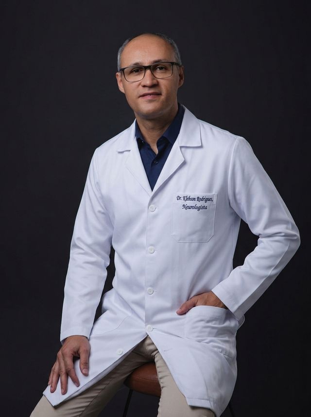 Dr. Klebson Rodrigues sentado, de jaleco, com a mão no bolso